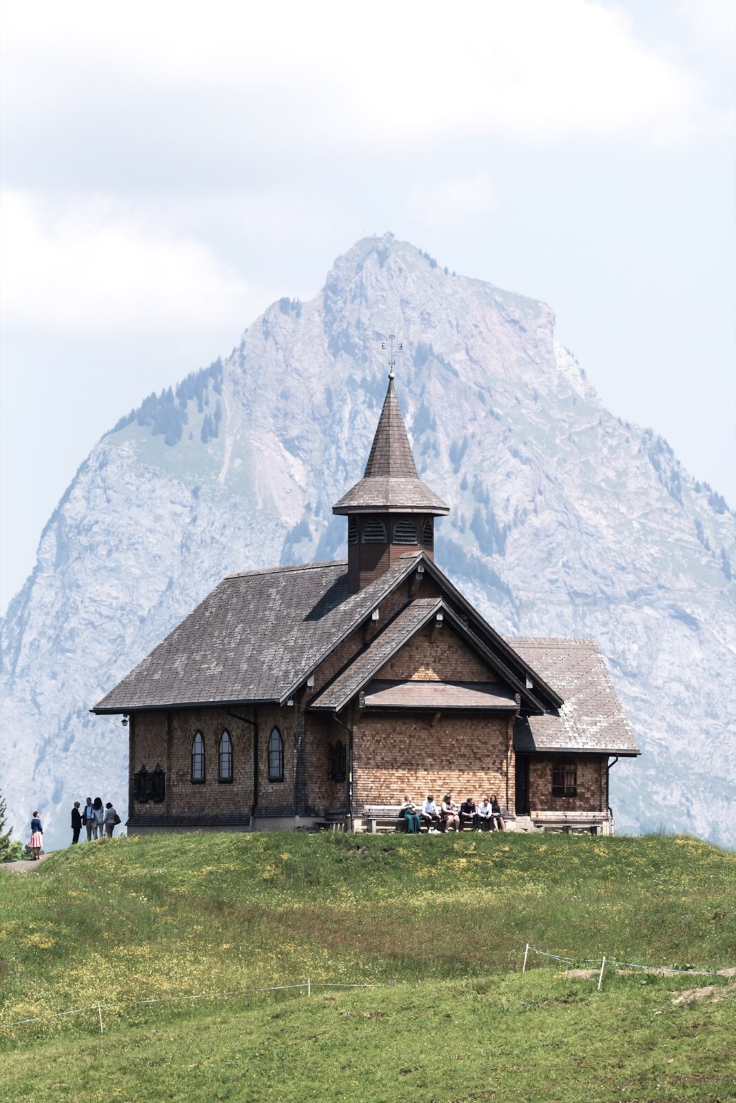 A chapel on a hilltop in front of a mountain in Switzerland